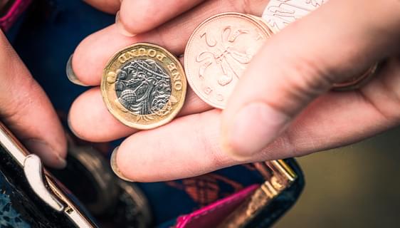 A photograph of a woman's hand holding a pound coin, a 20p and a 2p, taking them out of a blue purse