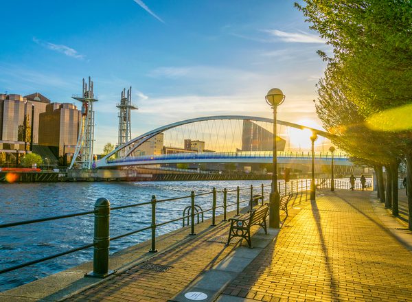 A rising sun shines through a view of a bridge over the water at Salford Quays
