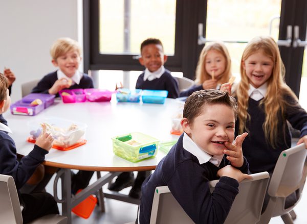 A group of children sit around a table at primary school. A little boy smiles into the camera
