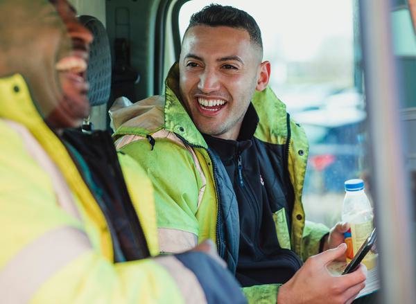 Two male construction workers in high vis jackets laughing together in a van