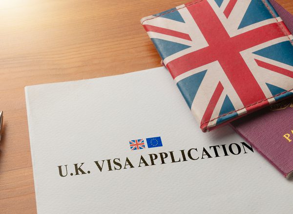 A form with the title 'UK Visa Application' sits on a desk next to a passport in a union jack cover