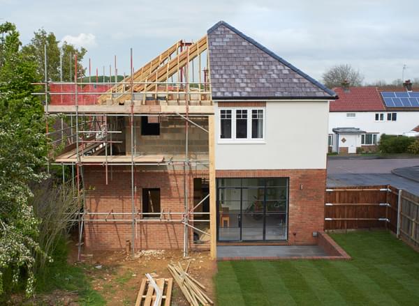 A house halfway through being built: half of it is complete and the other half reveals exposed timbers and scaffolding