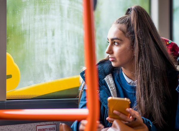 A young woman with a long ponytail sits looking out of a bus window