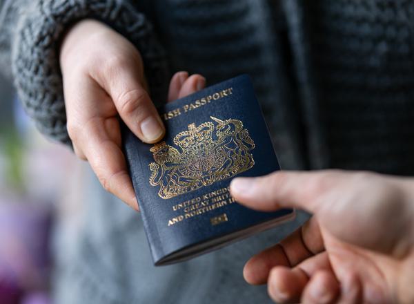 One person handing a blue UK passport to another