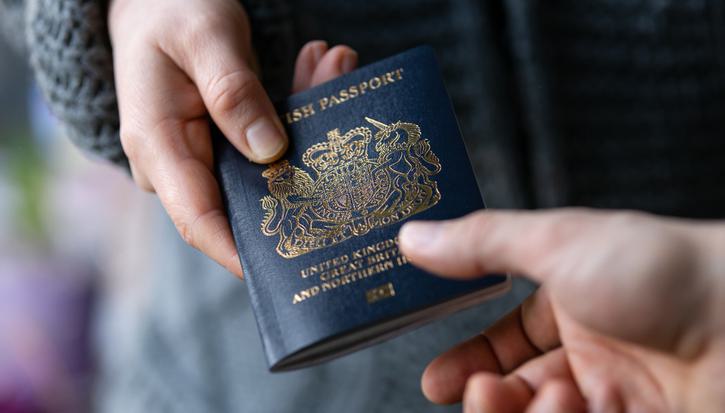 One person handing a blue UK passport to another