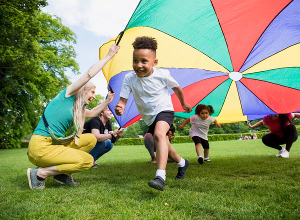 Two young children run playing underneath a rainbow canopy in a park or garden
