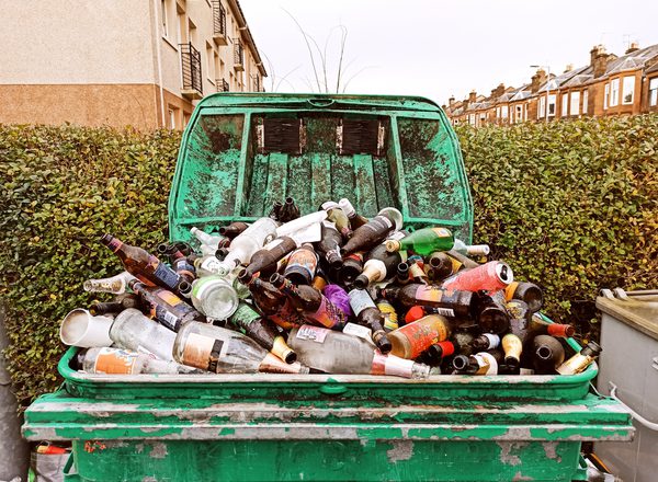 A huge overflowing recycling bin full of discarded empty bottles of alcoholic drinks