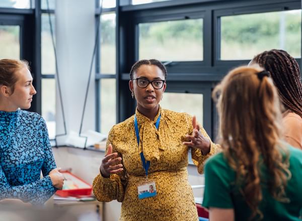 A secondary school teacher talking with her sixth form students in class.