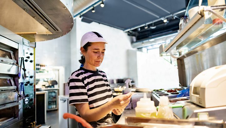 A woman in a white cap and black and white stripe t-shirt works in a restaurant kitchen