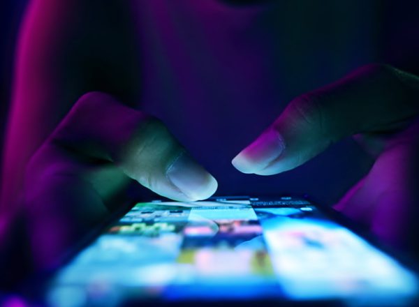 A close up photo of a lit up mobile phone screen. A woman's hands hold it, mostly in darkness