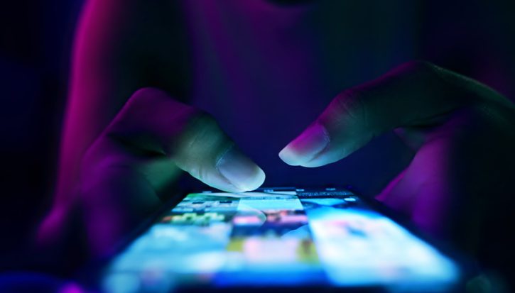 A close up photo of a lit up mobile phone screen. A woman's hands hold it, mostly in darkness