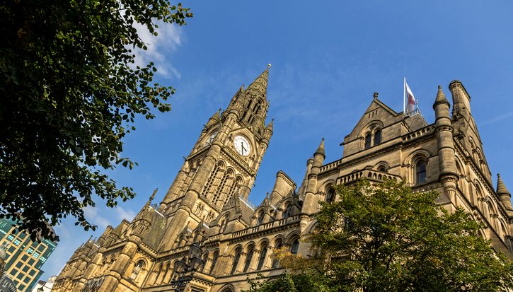 A photograph from below of the grand Manchester town hall building on a sunny day against a blue sky