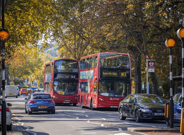 A two way street with busy traffic of driving cars and double-decker buses in autumn