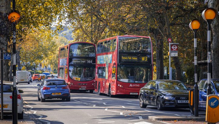 A two way street with busy traffic of driving cars and double-decker buses in autumn