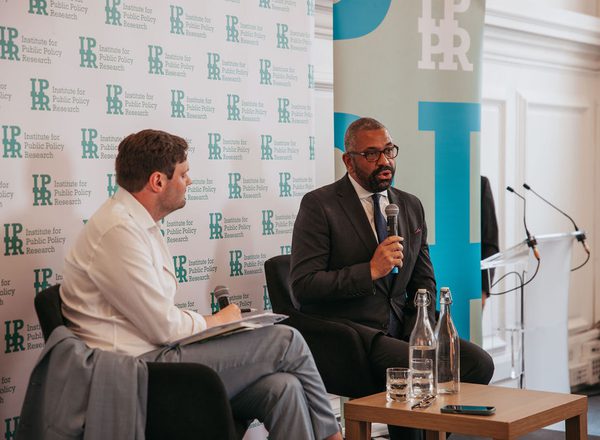 James Cleverly and Harry Quilter-Pinner sat in front of IPPR banners. James Cleverly is speaking into a microphone.